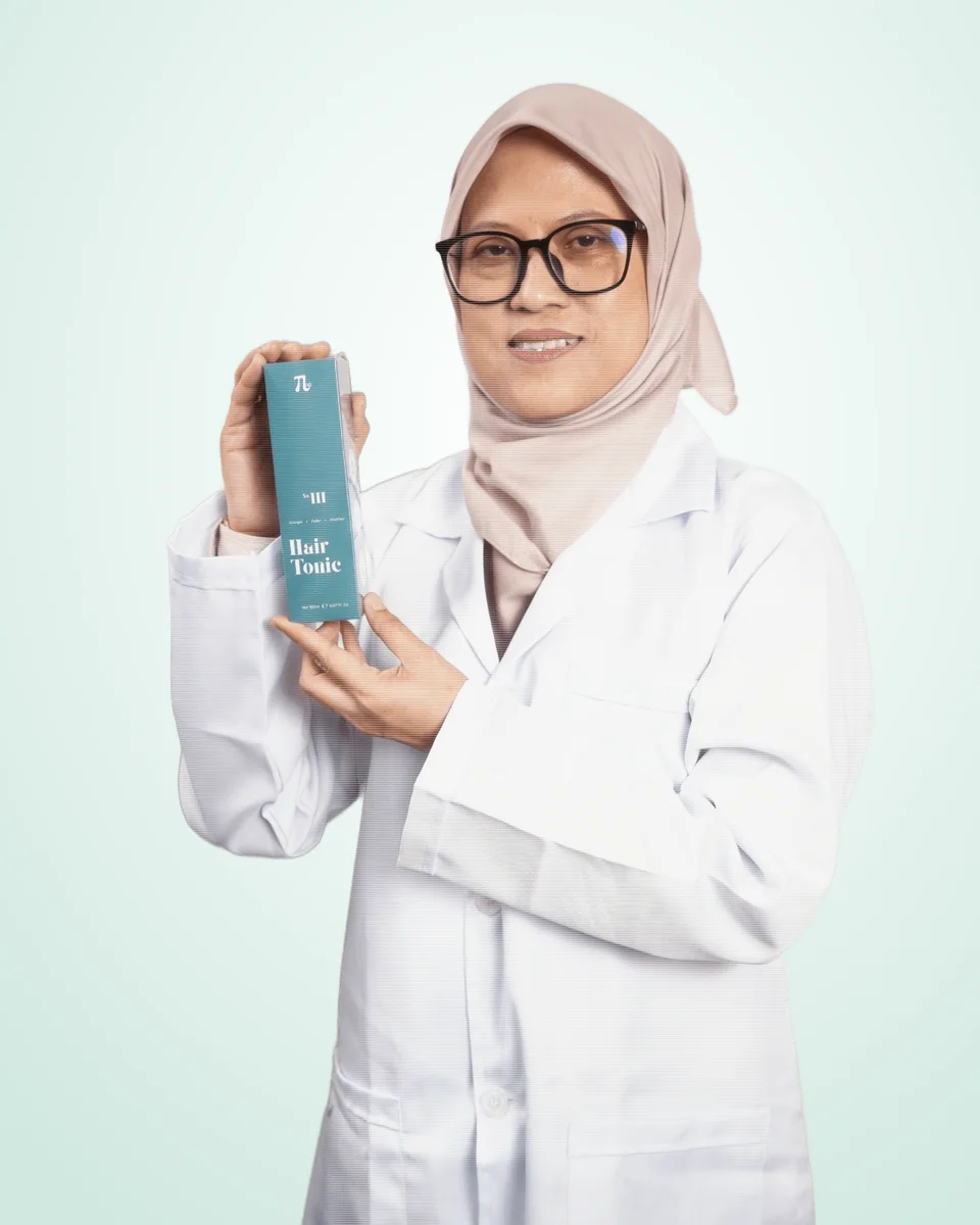 Assoc. Prof. Ir. Ts. Dr. Rosnani Hasham in a lab coat, holding a box of T·Lab Hair Tonic